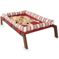 Small dog sleeping on a red elevated pet bed with striped cushion and wooden legs