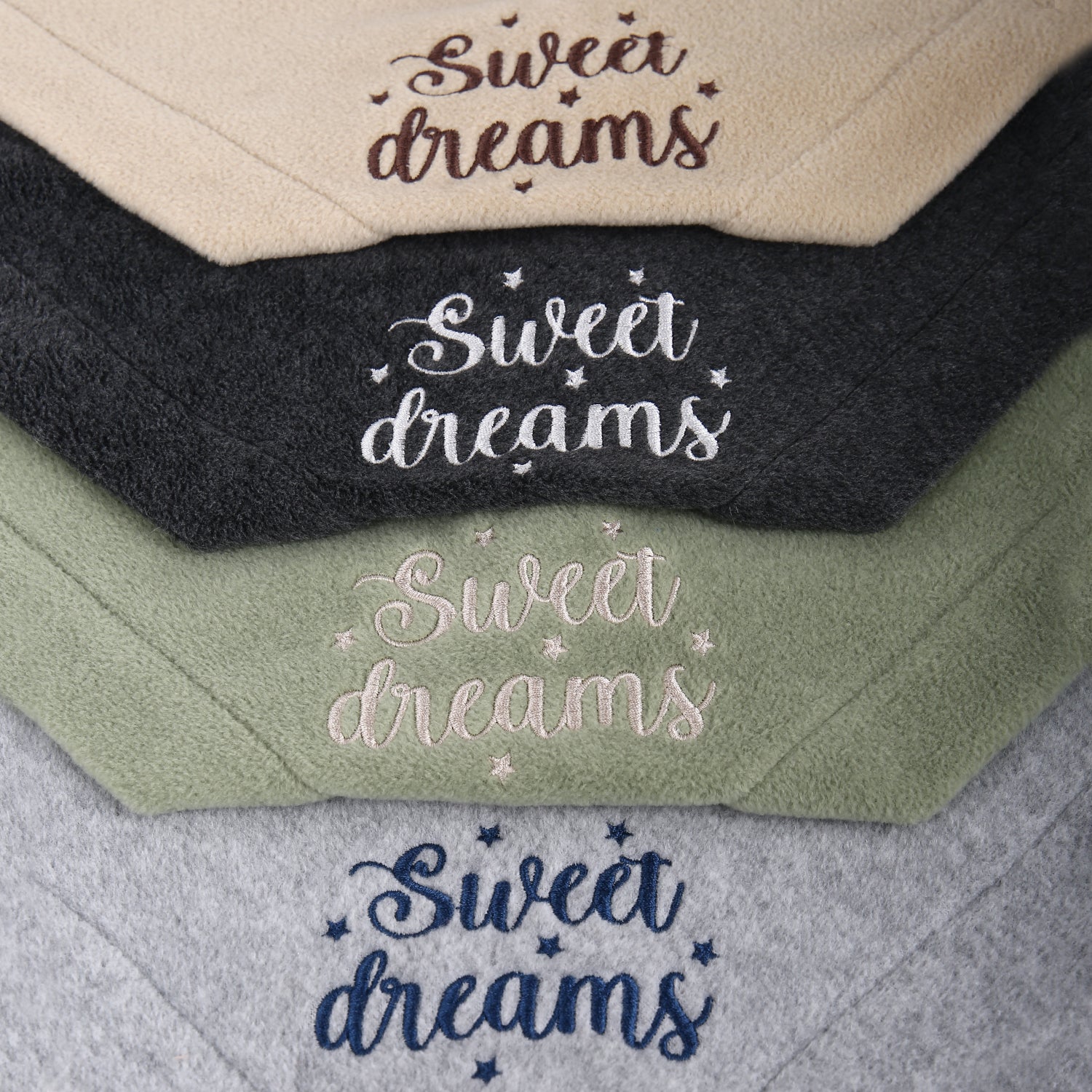 Stack of embroidered fleece blankets in beige, black, green, and gray with 'Sweet dreams' text.