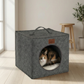Calico cat resting inside a gray felt cube cat house on light wood floor in a modern room