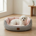Small white dog resting in a grey and pink plush pet bed on a wooden floor