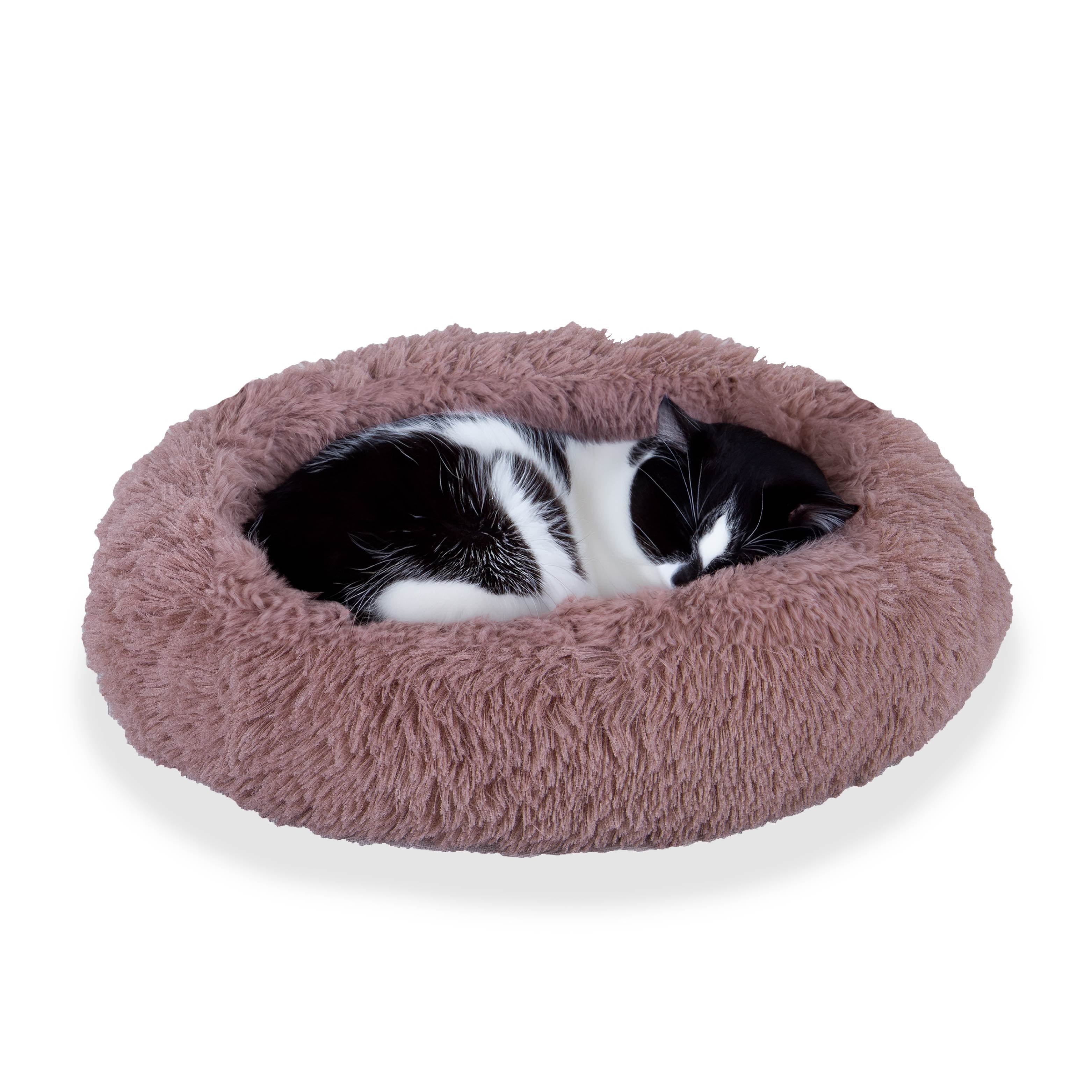 Black and white cat sleeping in a round, pink fluffy pet bed on white background